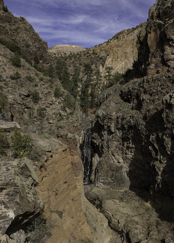 A waterfall flows in an orange-cliffed canyon.
