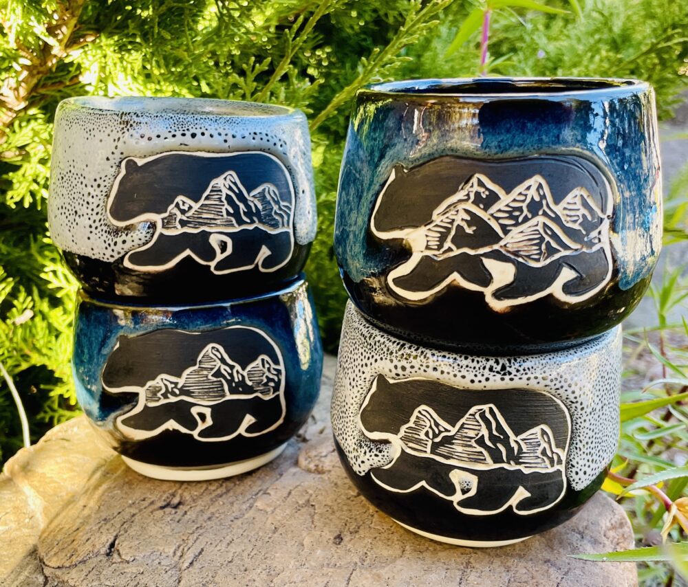 Four mugs with a bear design carved in them. They are in two stacks, with two mugs per stack.