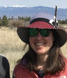 A woman wearing a hat a sunglasses with mountains in the background